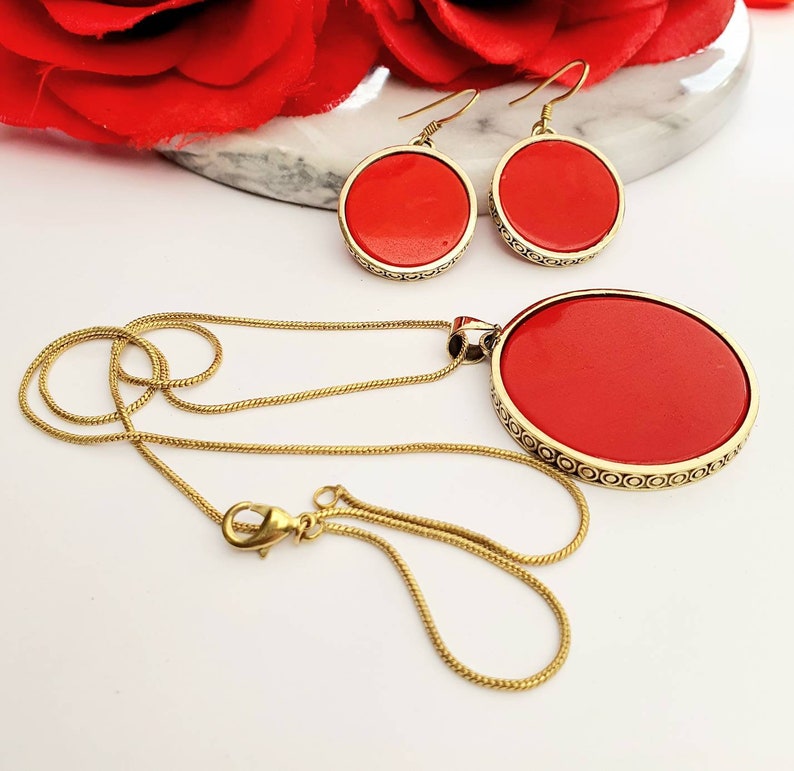 May include: A gold chain necklace with a large red pendant and matching red circle earrings. The pendant and earrings have a gold filigree design.