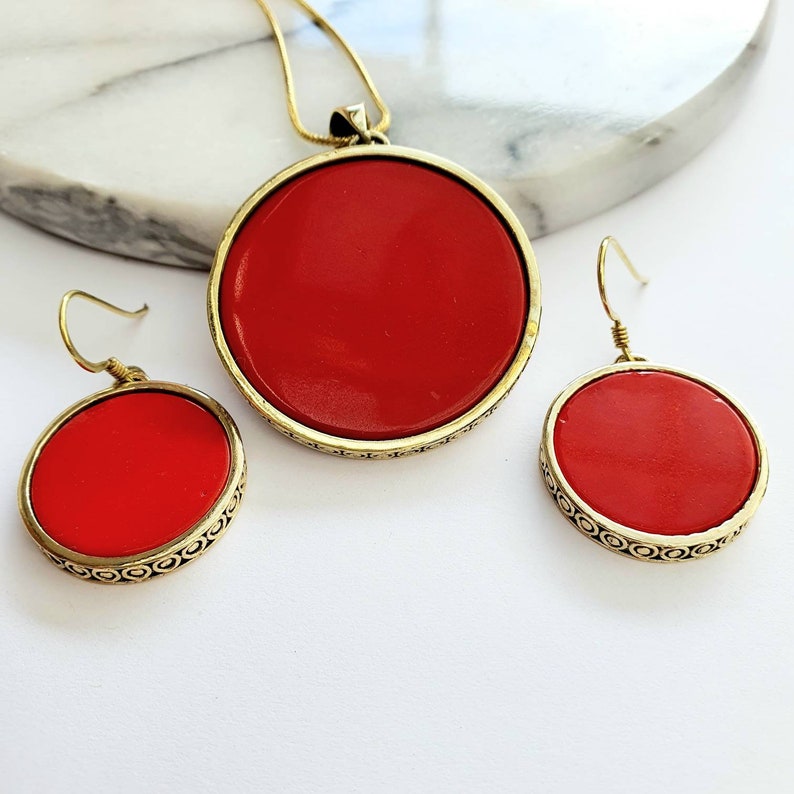 May include: A red and gold necklace and earrings set. The necklace features a large, round pendant with a red stone and a gold filigree design. The earrings are also round with red stones and gold filigree designs.
