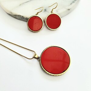 May include: A gold necklace and earrings set with red round pendants. The necklace has a delicate chain and the earrings have a simple hook closure.