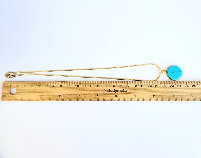 Peut inclure: Un collier en cha&icirc;ne dor&eacute;e avec un pendentif turquoise. Le pendentif est un disque rond et plat avec un motif marbr&eacute; bleu clair et blanc.