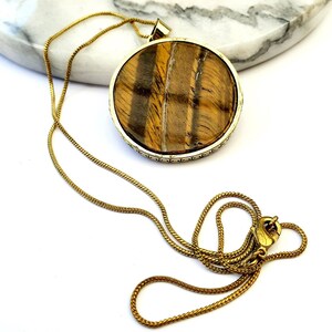 May include: A gold chain necklace with a large round pendant featuring a tiger's eye stone.