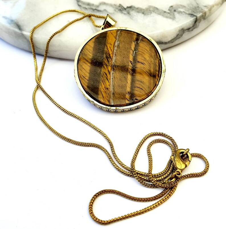 May include: A gold chain necklace with a large round pendant featuring a tiger's eye stone.