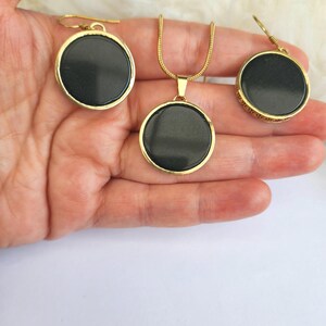 Puede incluir: Un conjunto de collar y pendientes de oro con colgantes redondos negros. Los colgantes tienen una superficie lisa y brillante.
