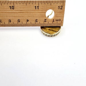 May include: A round, gold-toned pendant with a tiger's eye stone. The pendant is approximately 1 cm in diameter and has a decorative border.