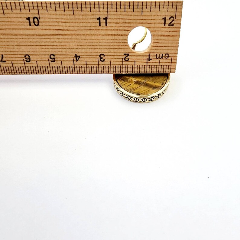 May include: A round, gold-toned pendant with a tiger's eye stone. The pendant is approximately 1 cm in diameter and has a decorative border.