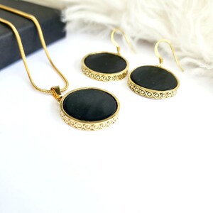 Puede incluir: Un conjunto de collar y pendientes de oro con colgantes redondos negros. Los colgantes tienen un borde dorado decorativo.