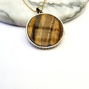 May include: Gold pendant necklace with a round tiger's eye stone.