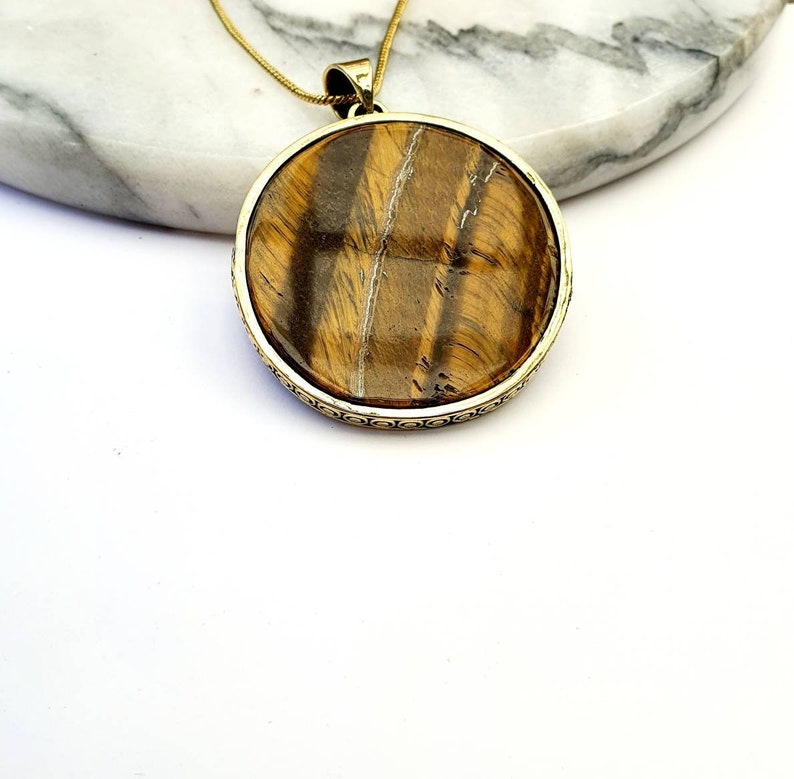 May include: Gold pendant necklace with a round tiger's eye stone.