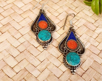 May include: A pair of silver dangle earrings with turquoise and coral stones. The earrings are in the shape of a teardrop and have intricate details.