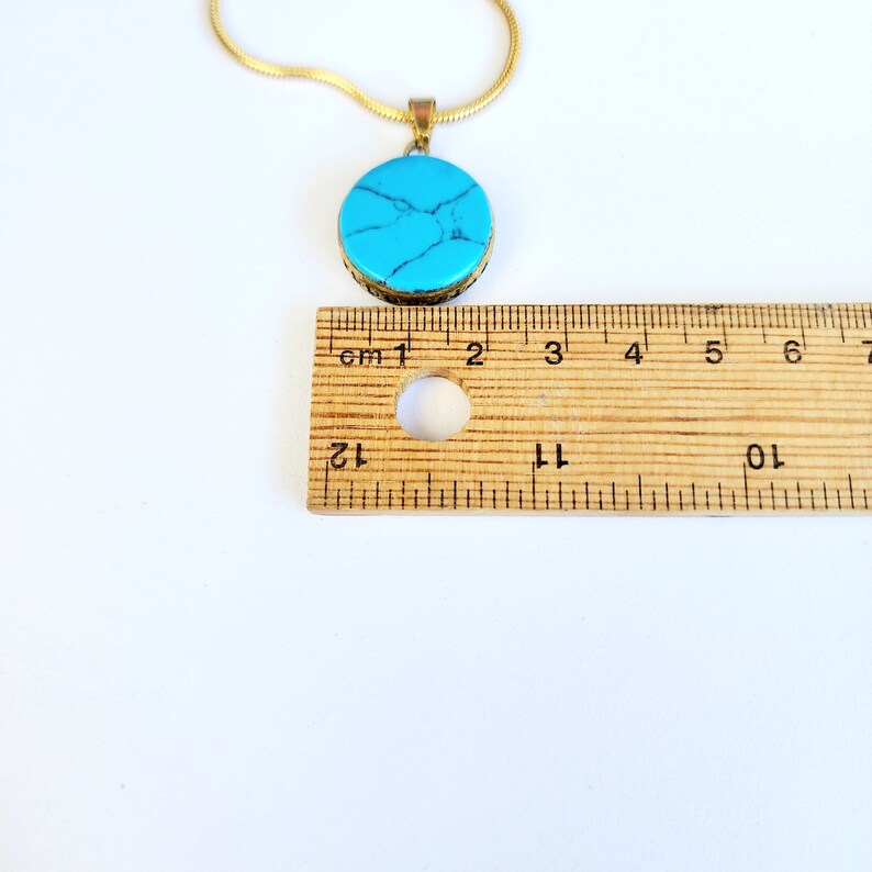 Peut inclure: Un collier avec un pendentif en pierre turquoise et une cha&icirc;ne dor&eacute;e. Le pendentif est rond et mesure environ 3,8 cm de diam&egrave;tre.