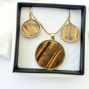 May include: A gold necklace and earrings set with round tiger's eye stones. The stones have a brown and gold color with a striated pattern.