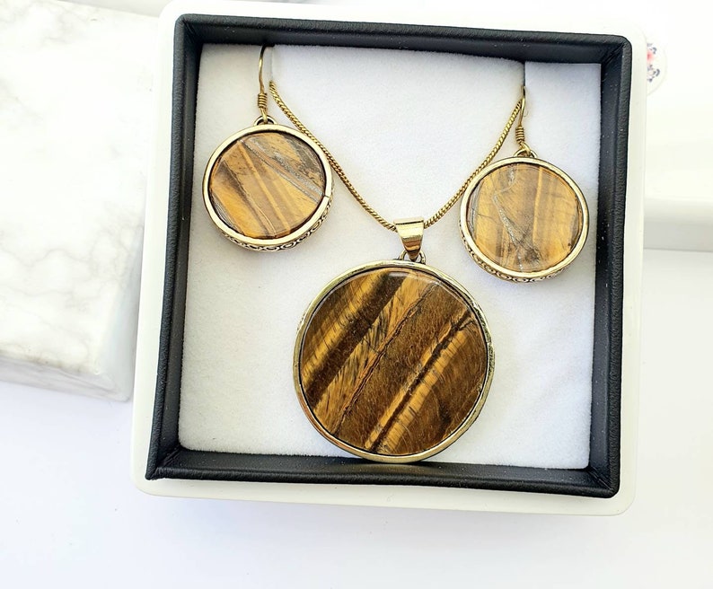 May include: A gold necklace and earrings set with round tiger's eye stones. The stones have a brown and gold color with a striated pattern.