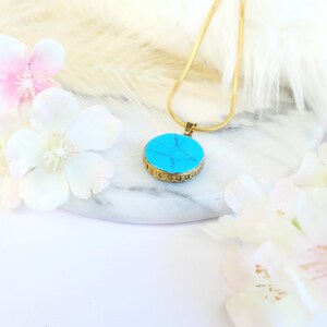 Peut inclure: Un collier en cha&icirc;ne dor&eacute;e avec un pendentif rond bleu turquoise. Le pendentif est orn&eacute; d'un motif de filigrane dor&eacute; sur le bord.