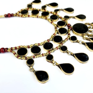 May include: A gold necklace with black round and teardrop-shaped beads. The necklace has a layered design with multiple strands of beads.