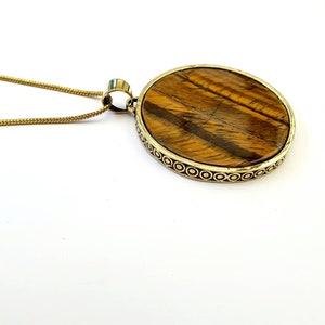 May include: A gold chain necklace with a round pendant featuring a tiger's eye stone set in a gold-toned metal frame.