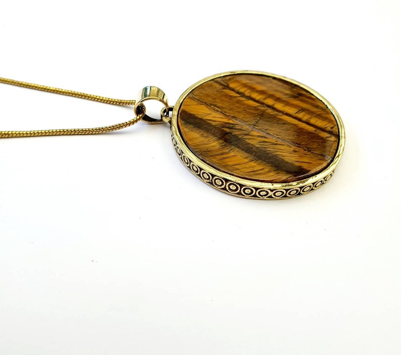 May include: A gold chain necklace with a round pendant featuring a tiger's eye stone set in a gold-toned metal frame.