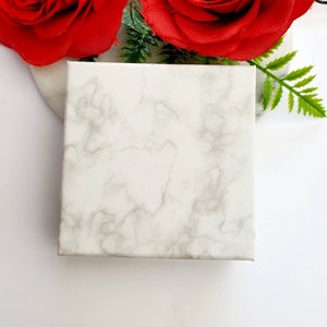 May include: A white marble-patterned gift box with a smooth surface. The box is empty and ready to be filled with a special gift.