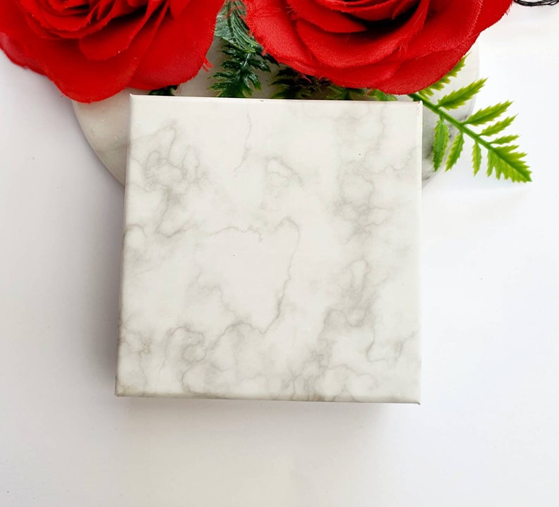 May include: A white marble-patterned gift box with a smooth surface. The box is empty and ready to be filled with a special gift.