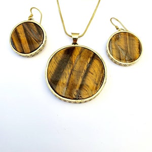 May include: A gold necklace and earrings set with round tiger's eye stone pendants.