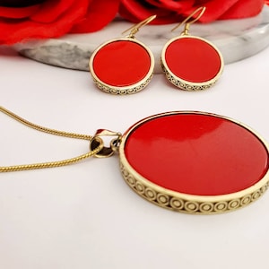 May include: A red and gold necklace and earrings set. The necklace has a round pendant with a red center and a gold border. The earrings are also round with a red center and a gold border.