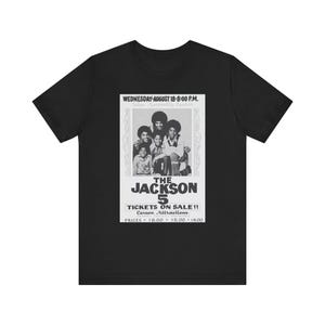 May include: Black t-shirt with a vintage concert poster design for The Jackson 5. The poster includes the band's name, a group photo, and event details: Wednesday, August 18, 8:00 PM, and ticket prices.