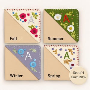 May include: Set of four embroidered corner bookmarks, each representing a season: Fall, Summer, Winter, and Spring. Each bookmark features a floral design, the letter "A", and a stitched border. The "Set of 4 Save 20%" text is in the lower right corner.