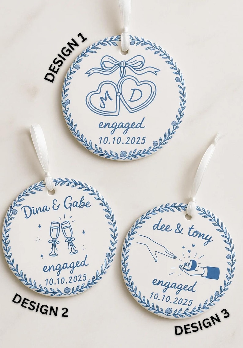 May include: Three white ceramic engagement ornaments with blue designs and white ribbons. Design 1 features intertwined hearts with initials and the date. Design 2 shows champagne flutes. Design 3 depicts a proposal.