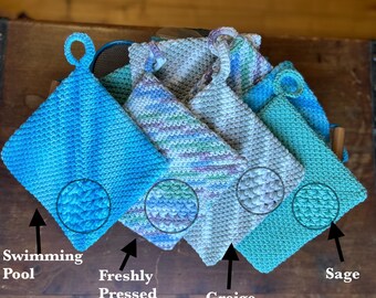 Puede incluir: Cinco agarraderas de olla de ganchillo en varios tonos de azul y verde. Las agarraderas están hechas con un punto texturizado y tienen un lazo para colgar. Los colores están etiquetados como "Piscina", "Recién exprimido", "Grises", "Salvia".