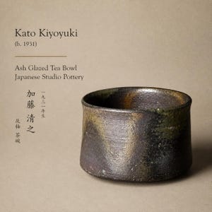 May include: An ash-glazed tea bowl by Kato Kiyoyuki, Japanese Studio Pottery. The bowl has a dark, textured exterior with hints of green and brown. The text on the image reads "Kato Kiyoyuki (b. 1931)" and "Ash Glazed Tea Bowl Japanese Studio Pottery."