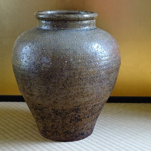 May include: A large, brown ceramic vase with a speckled glaze. The vase has a rounded body and a wide mouth.