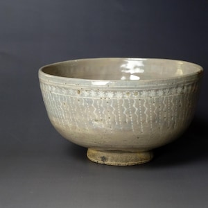 Puede incluir: Un cuenco de cerámica blanca con un diseño decorativo alrededor del borde. El cuenco tiene una forma ancha y redonda y un pequeño pie.