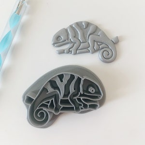 May include: Two silver-coloured chameleon cookie cutters. One is a solid design and the other is a detailed outline.
