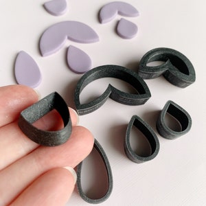 May include: A set of polymer clay cutters in black and purple. The cutters are shaped like teardrops, half circles, and a combination of both.