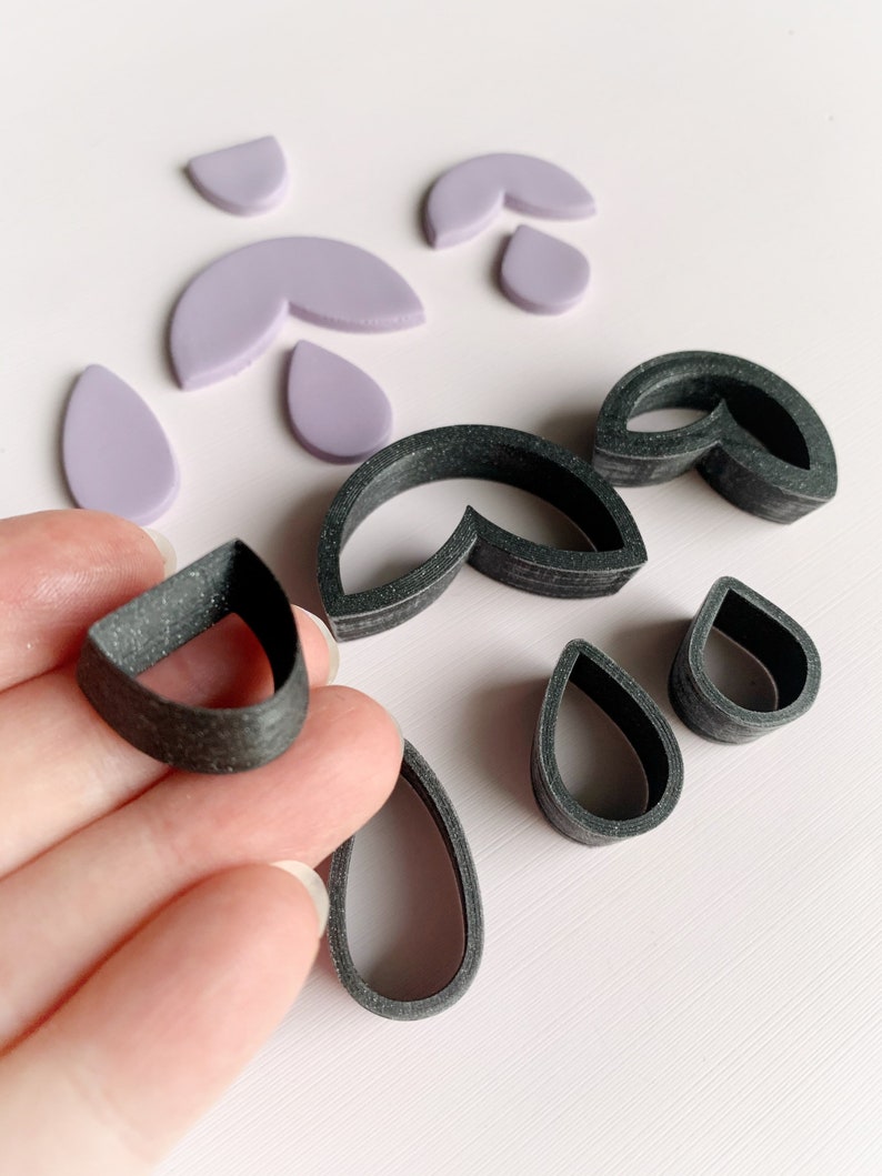 May include: A set of polymer clay cutters in black and purple. The cutters are shaped like teardrops, half circles, and a combination of both.