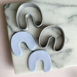 May include: Two gray silicone cookie cutters shaped like a horseshoe with a curved line in the middle, and two light blue silicone cookie cutters shaped like a horseshoe.
