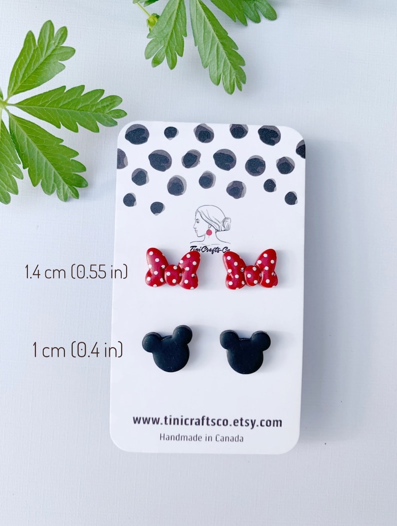 May include: A set of four polymer clay earrings. Two red and white polka dot bow earrings, each measuring 1.4 cm in diameter. Two black Mickey Mouse head earrings, each measuring 1 cm in diameter. The earrings are displayed on a white card with black polka dots. The card also includes the text "Tini Crafts-Co", "1.4 cm (0.55 in)", "1 cm (0.4 in)", "www.tinicraftsco.etsy.com", and "Handmade in Canada".
