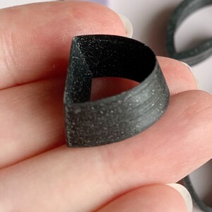 May include: A black plastic ring with a textured surface. The ring is designed to be worn on the finger.