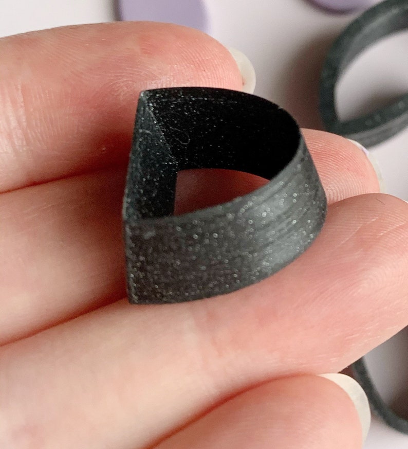 May include: A black plastic ring with a textured surface. The ring is designed to be worn on the finger.