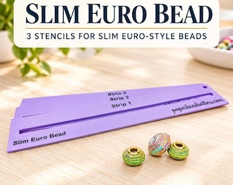 May include: Three purple plastic stencils for crafting slim euro-style beads, labeled Strip 1, Strip 2, and Strip 3, with the text Slim Euro Bead and paperbeadrollers.com. Three finished colorful beads with gold metal cores sit nearby.
