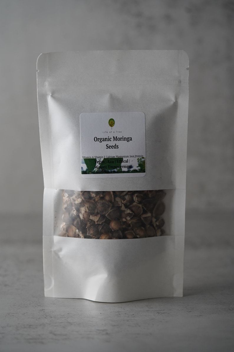 Puede incluir: Una bolsa blanca resellable con una etiqueta que dice "Organic Moringa Seeds" y enumera los beneficios nutricionales de las semillas de moringa. La bolsa contiene semillas de moringa marrones.