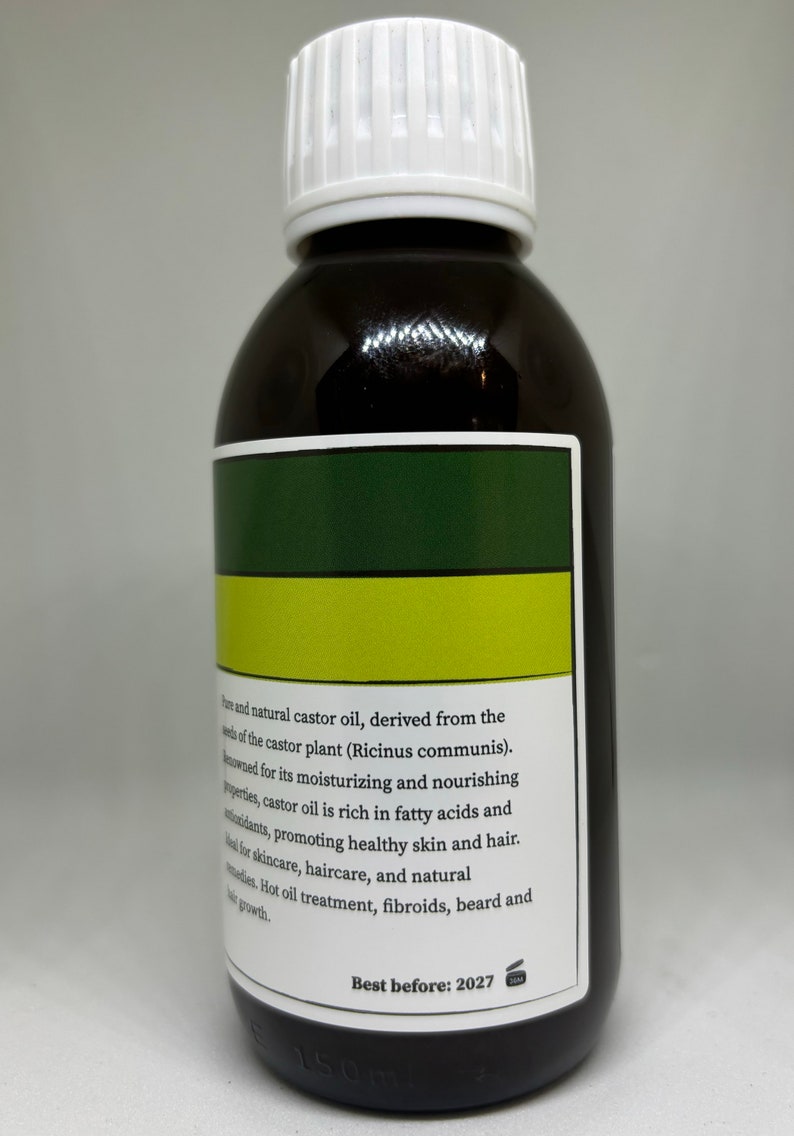 Op de afbeelding: Een donkerbruine fles ricinusolie met een witte dop. Het etiket heeft groene en gele strepen en tekst die de voordelen van de olie voor huid en haar beschrijft. De fles bevat 150 ml en is houdbaar tot 2027.