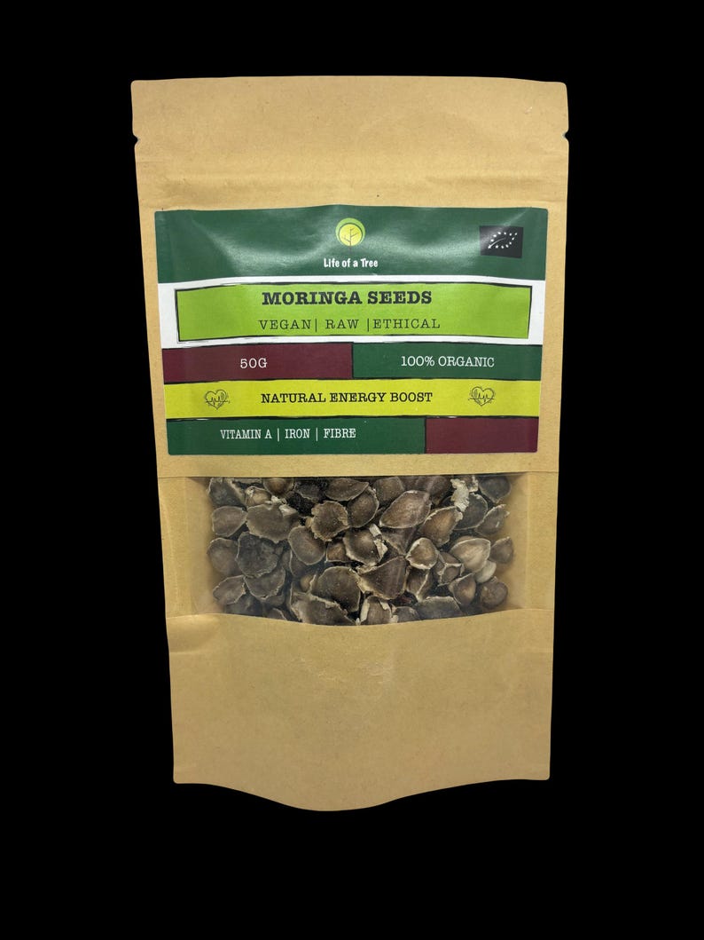 Puede incluir: Una bolsa de papel marr&oacute;n con una ventana transparente que muestra semillas de moringa. La bolsa tiene una etiqueta que dice "Life of a Tree Moringa Seeds Vegan Raw Ethical 50g 100% Organic Natural Energy Boost Vitamin A Iron Fibre".