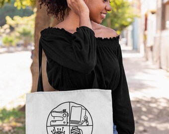 May include: White tote bag with a black circle design featuring sewing icons like a sewing machine, fabric, needles, and thread. The text "Sewing Adventures Await" is printed below the circle.