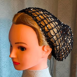 May include: Black hair net with white beads, worn on a mannequin head. The net is made of a fine mesh material and has a gathered bun shape.