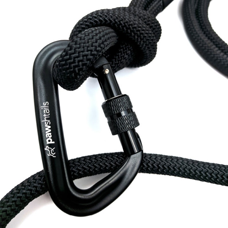 May include: Black rope dog leash with a black metal carabiner clip. The carabiner has the word "pawshtails" engraved on it.