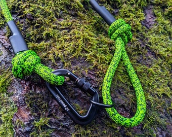 May include: A green and black rope dog leash with a black metal clip. The leash is made of a durable, braided rope and has a strong, secure clip. The leash is shown against a background of green moss.