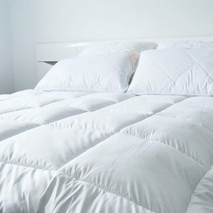 May include: A white bed with a white comforter and two white pillows. The comforter has a quilted design.