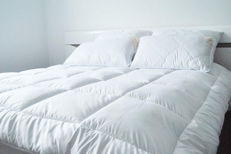 May include: A white bed with a white comforter and two white pillows. The comforter has a quilted design.