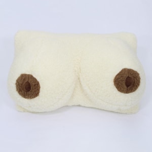 Può includere: Un cuscino di peluche bianco a forma di un paio di seni con capezzoli in feltro marrone.