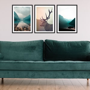 May include: Three framed landscape photographs of a lake and mountains, a deer, and a lake and mountains. The photographs are hanging on a white wall above a teal green velvet sofa.